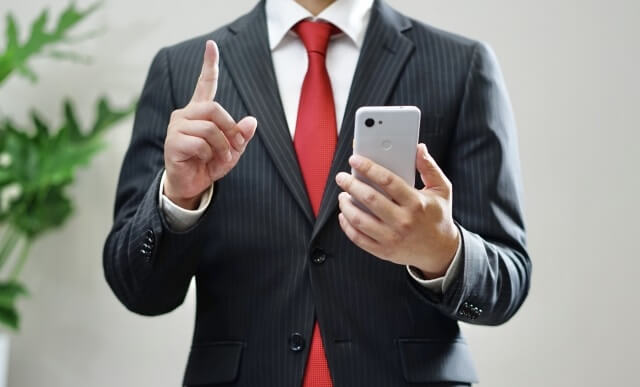 スマホを持って指を指すビジネスマン