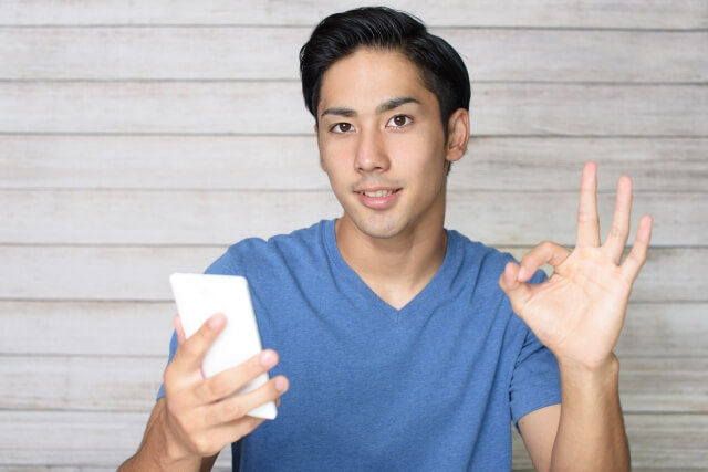 スマホを持ちOKサインをする男性