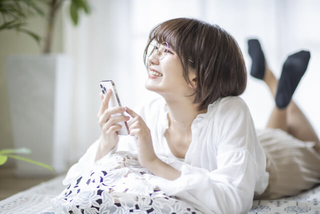 寝転がって笑顔でスマホを扱う女性
