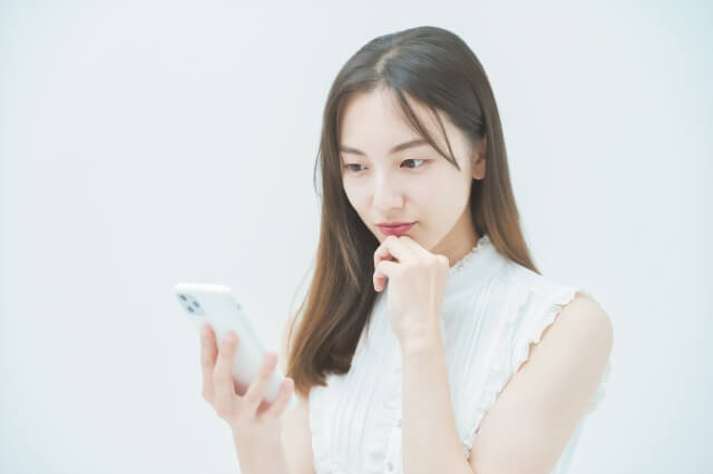 スマホを持ち考える女性