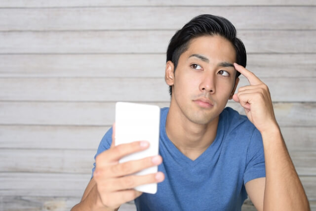 スマホを持ち考えている男性