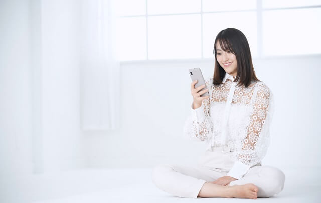 あぐらをかいて座っている女性が笑顔でスマホを見ている