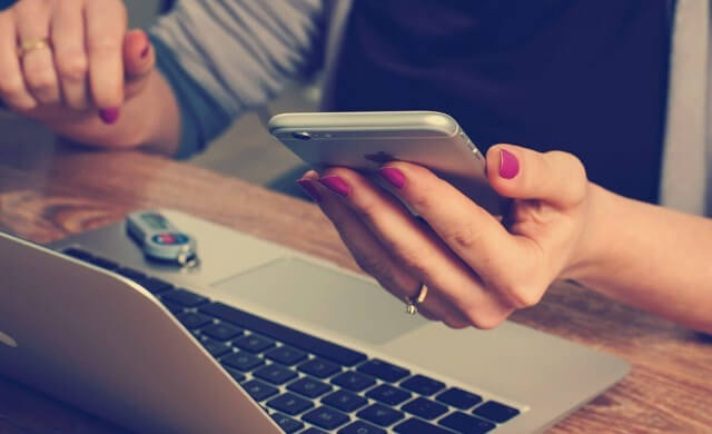 パソコンの前でスマホを見る女性の手