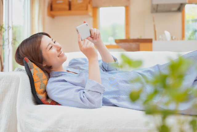 女性がソファに横になりスマホを見ている様子