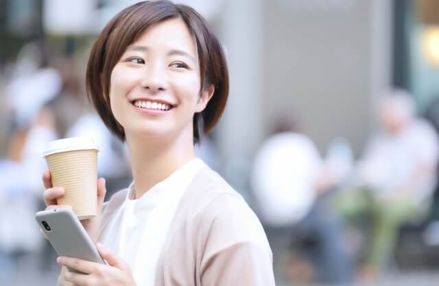 スマホを飲み物を持って町を歩く女性