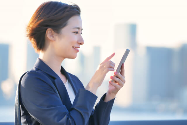スーツ姿の女性が外でスマホをいじっている様子