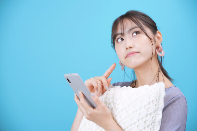 スマホを持ち考える女性