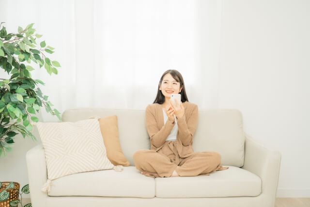 ソファでスマホを持ち笑顔になっている女性