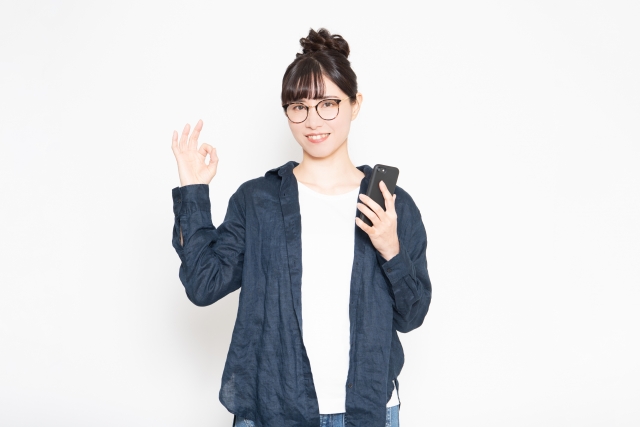 笑顔の女性がスマホをもってOKサインをしている様子