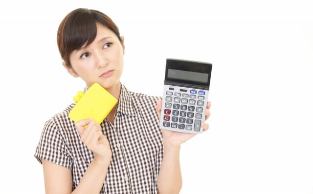 電卓と財布を持ち不安そうな女性